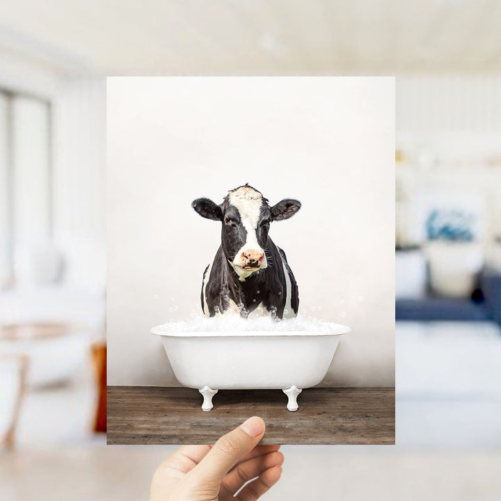 A black and white cow is sitting in a white bathtub filled with water, creating a whimsical and humorous scene.