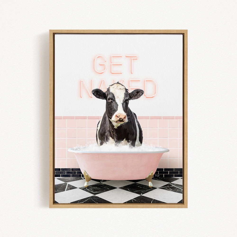 A black and white cow is sitting in a pink bathtub filled with water, with the words "GET NAKED" written in neon pink letters above the tub.