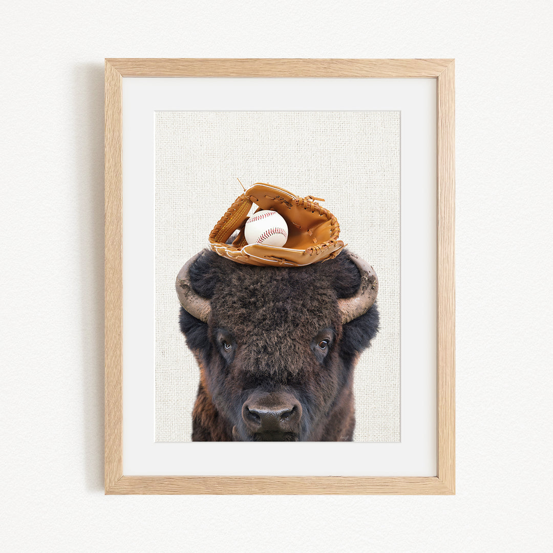 A framed image of a buffalo with a baseball glove on its head.