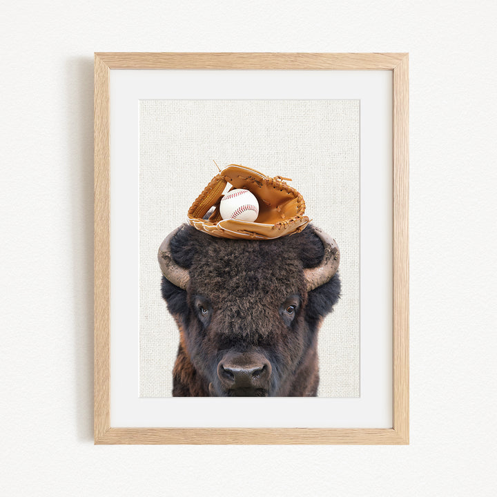 A framed image of a buffalo with a baseball glove on its head.
