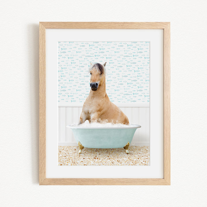 A light brown horse is sitting in a blue bathtub filled with water, surrounded by a patterned tile floor.