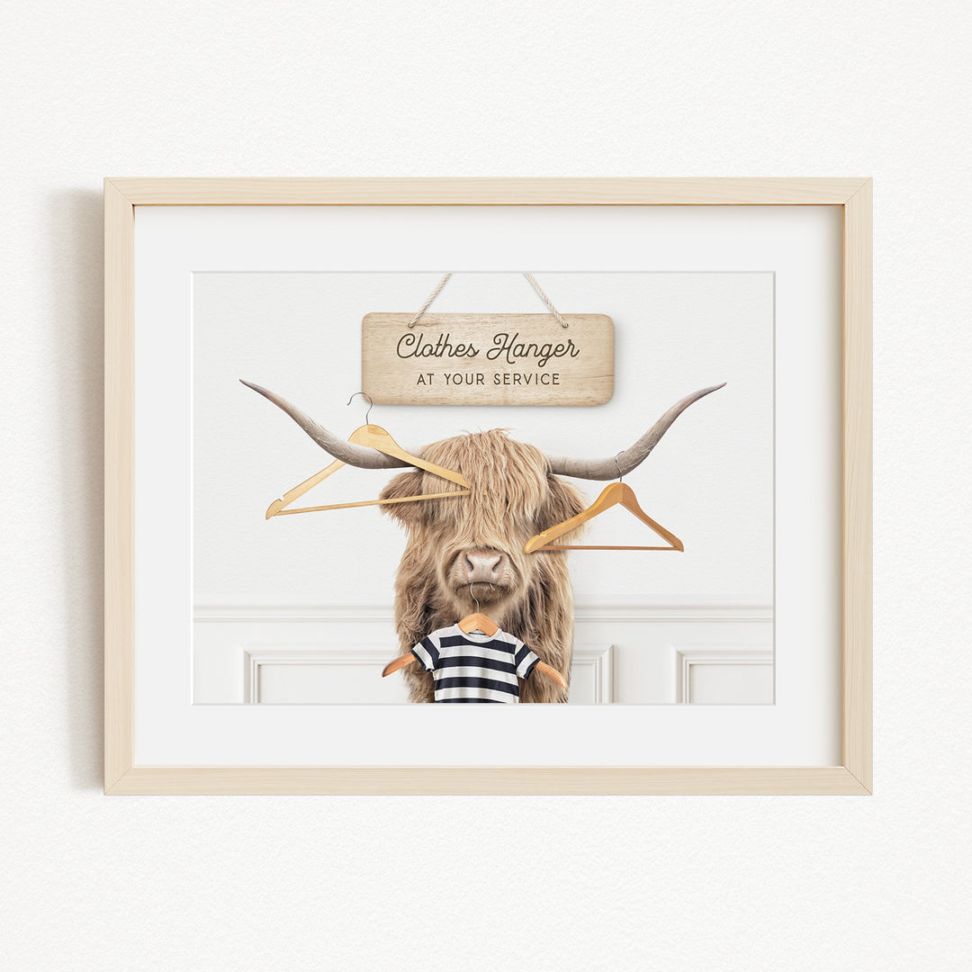 A framed image depicting a large, furry animal with a sign that reads "Clothes Hanger at your service" hanging above it.