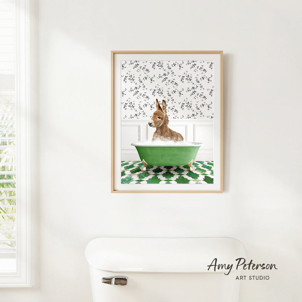 A framed print of a donkey sitting in a green bathtub is hanging on a white wall in a bathroom.