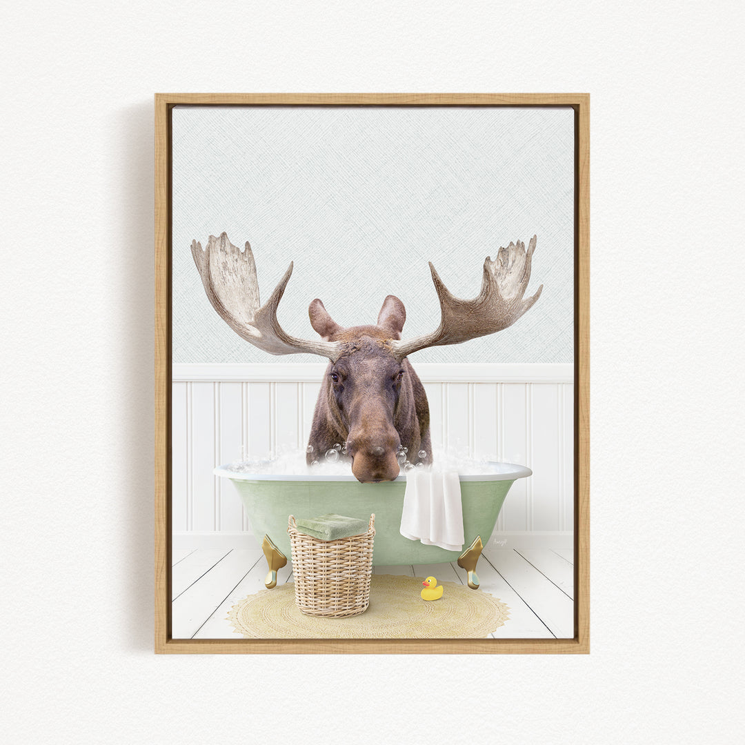 A moose with large antlers is sitting in a green bathtub filled with water, surrounded by a basket of toys and a yellow rubber duck.