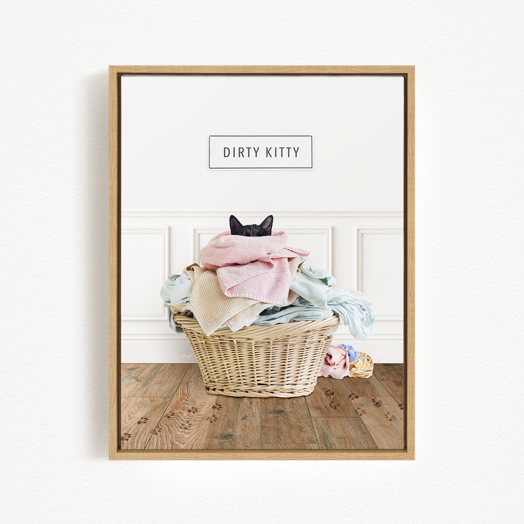 A framed image of a cat sitting in a basket filled with laundry, with the text "Dirty Kitty" displayed above the basket.