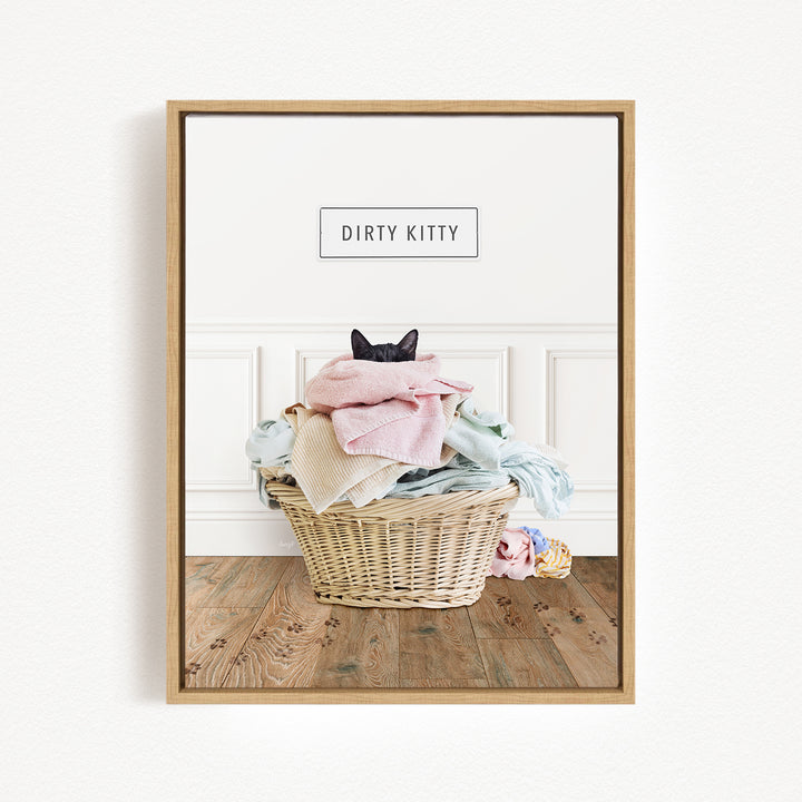 A framed image of a cat sitting in a basket filled with laundry, with the text "Dirty Kitty" displayed above the basket.