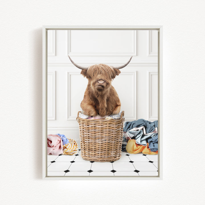 A Highland cow sits in a wicker basket filled with laundry, surrounded by various colorful clothes.
