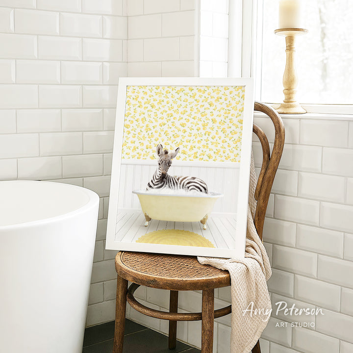 A framed image of a zebra sitting in a bathtub, with a yellow floral pattern on the wall behind it.