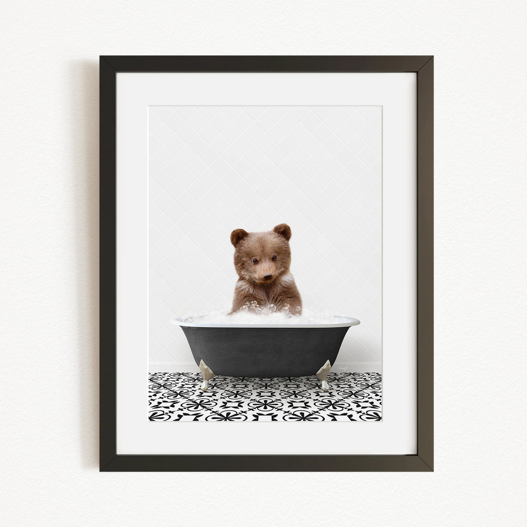 A cute brown bear cub sitting in a black bathtub filled with water, surrounded by a black and white patterned tile floor.