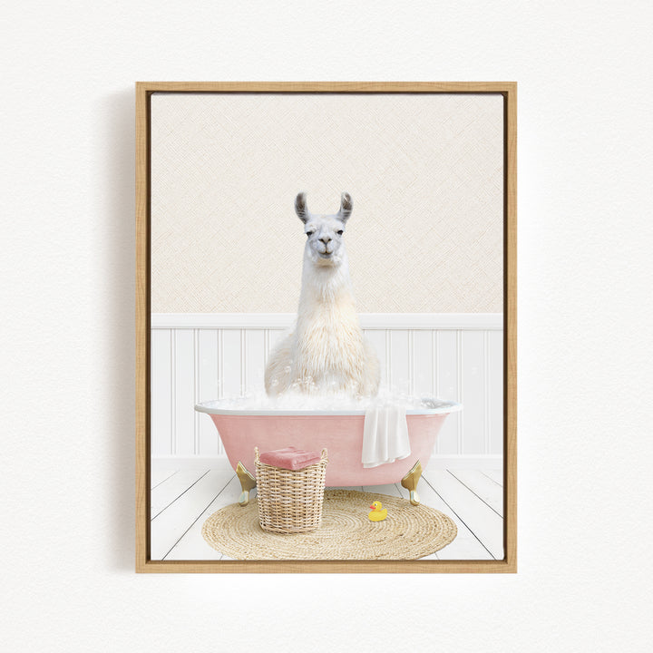 A white llama sitting in a pink bathtub filled with bubbles, surrounded by a basket of bath toys and a yellow rubber duck.