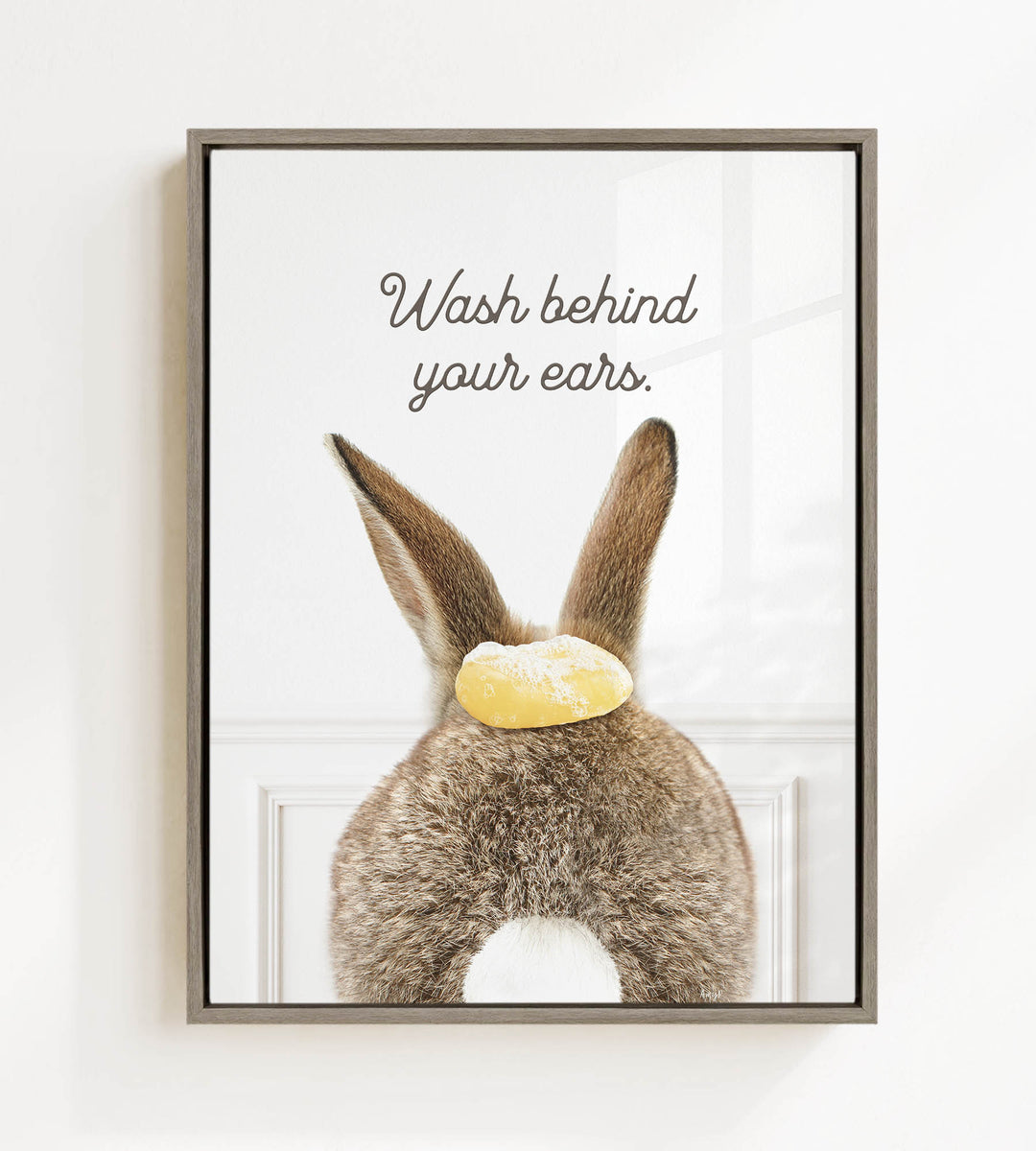 A framed image of a rabbit's ears with a yellow object on top, accompanied by the text "Wash behind your ears."