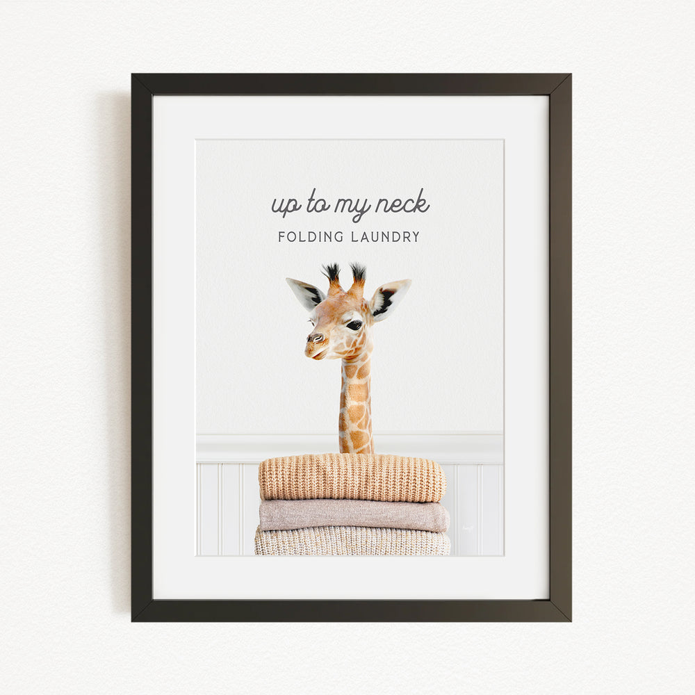 A framed image of a giraffe standing on top of folded laundry, with the text "up to my neck" and "Folding laundry" written above it.