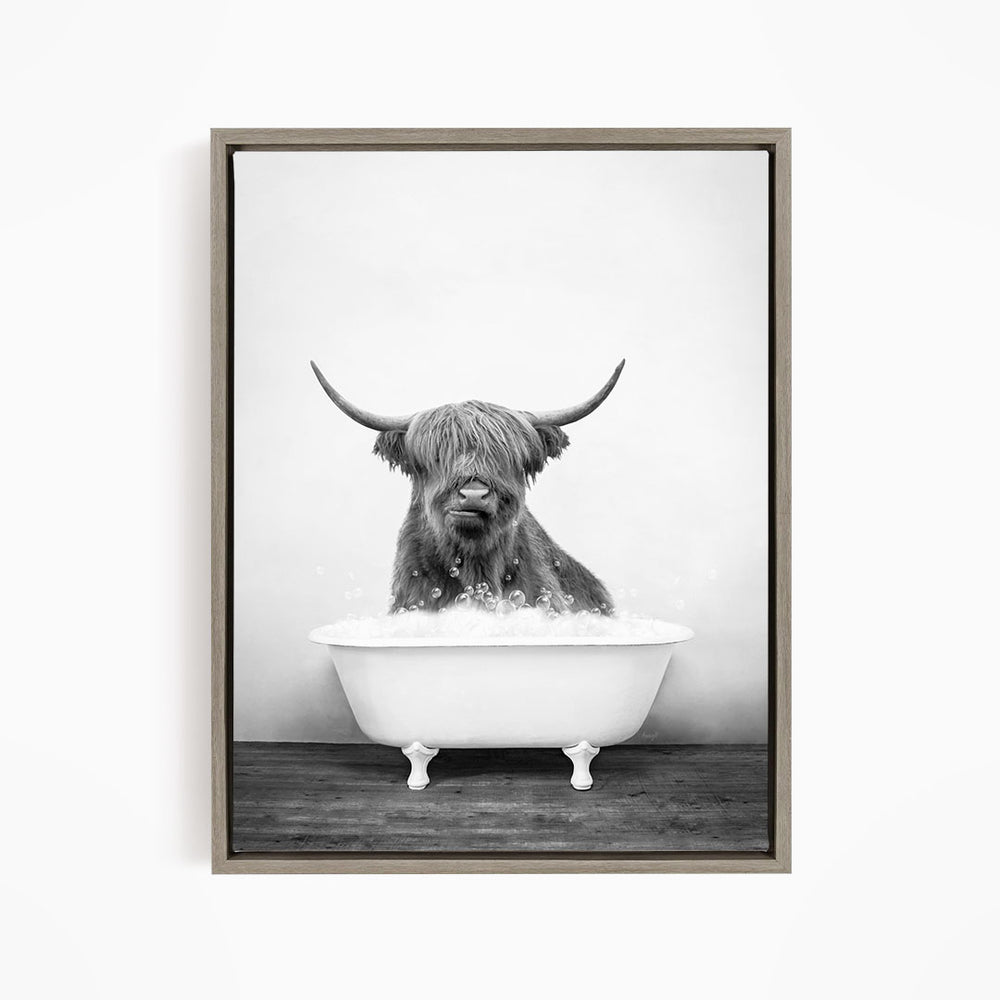 A black and white image of a Highland cow sitting in a bathtub filled with water, with its horns prominently displayed.