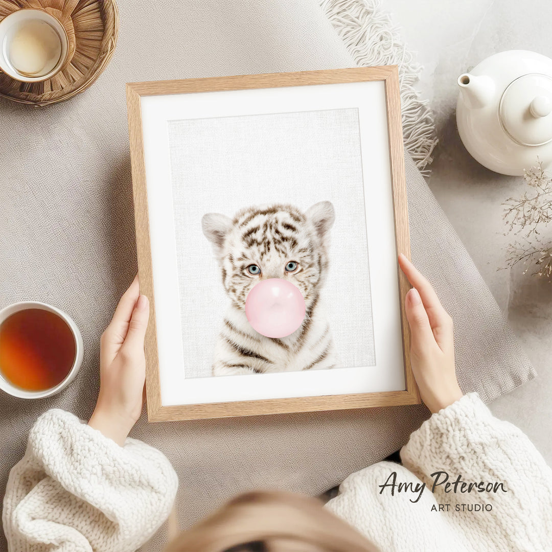 A person is holding a framed picture of a tiger blowing a bubble with a pink bubble gum bubble.