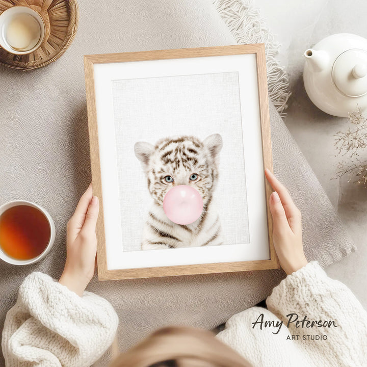 A person is holding a framed picture of a tiger blowing a bubble with a pink bubble gum bubble.