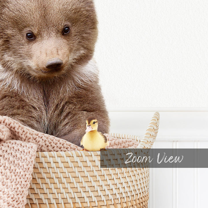 A brown bear sits in a woven basket, with a small yellow duck perched on its left side.