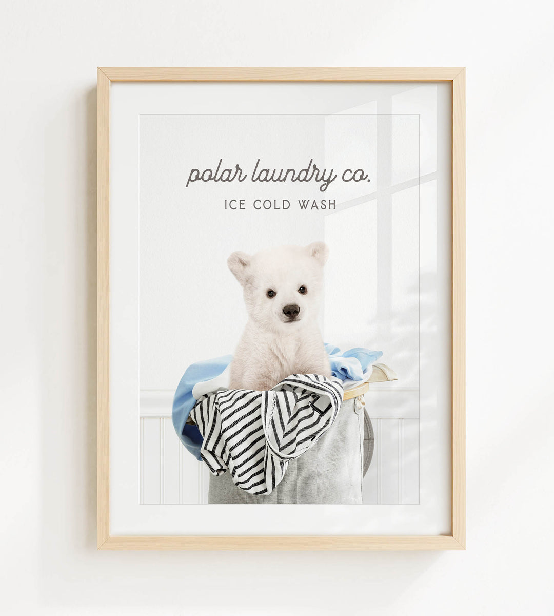 A framed image of a white dog sitting in a laundry basket filled with clothes, with the text "polar laundry co. ICE COLD WASH" displayed above the image.