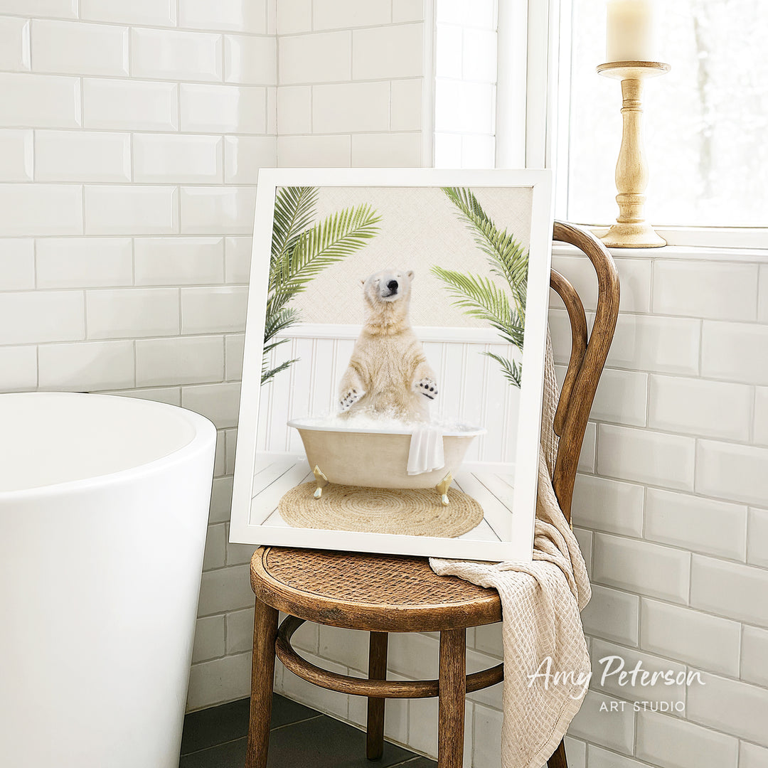 A framed image of a polar bear sitting in a bathtub, surrounded by palm leaves, is displayed on a wooden chair in a bathroom setting.