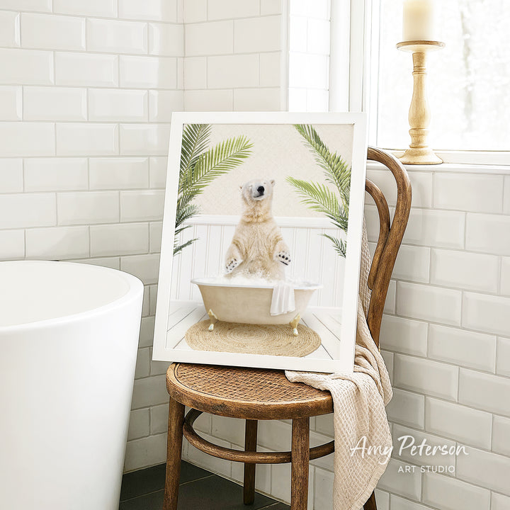 A framed image of a polar bear sitting in a bathtub, surrounded by palm leaves, is displayed on a wooden chair in a bathroom setting.