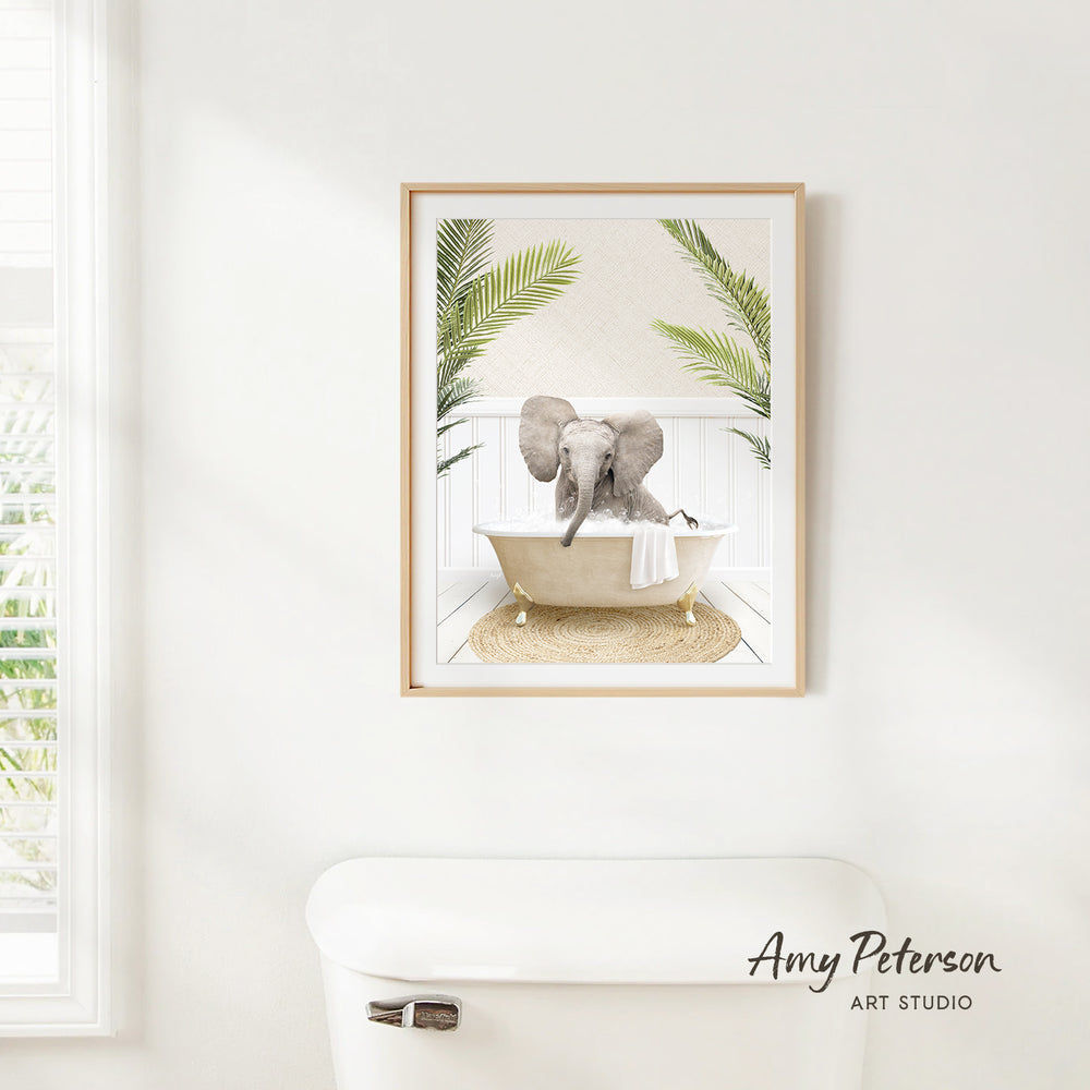 A framed image of an elephant sitting in a bathtub, surrounded by palm leaves, is hanging on a white wall in a bathroom.