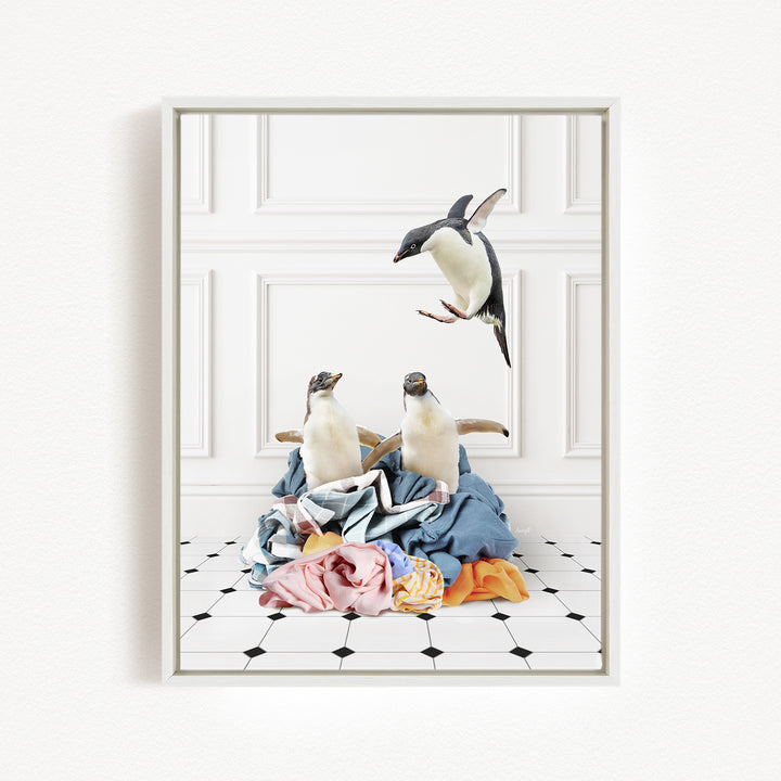 A framed photograph depicting two penguins standing on a pile of clothes, with one penguin flying towards the other.