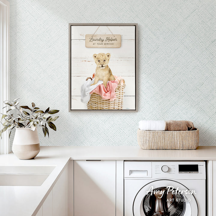 a laundry room with a framed poster of a baby lion in a basket, a white washing machine, and a potted plant on the counter.