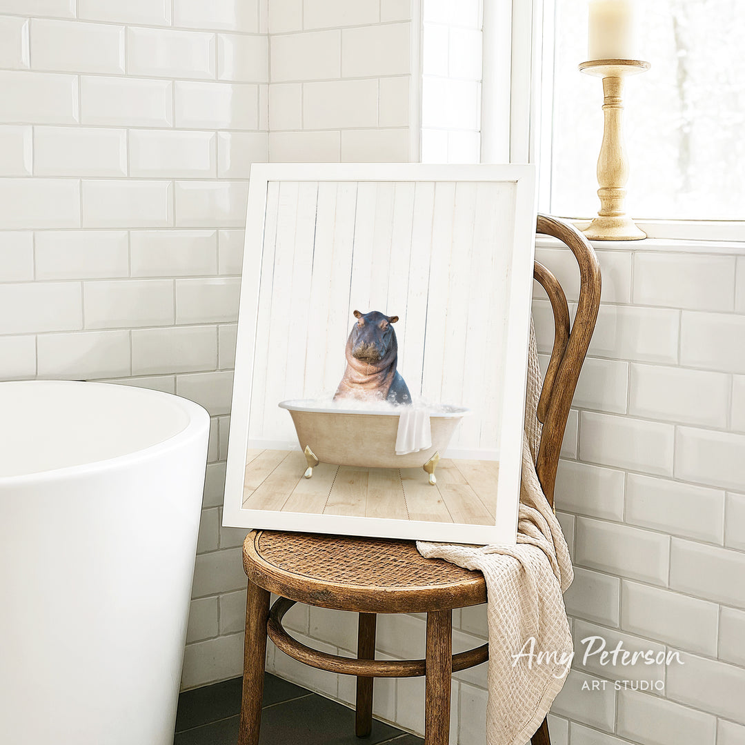 A framed image of a hippopotamus sitting in a bathtub is displayed on a wooden chair in a bathroom setting.
