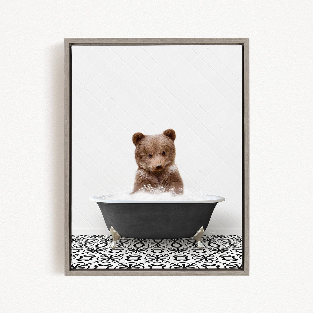 A cute brown bear cub sitting in a black bathtub filled with water, surrounded by a black and white patterned floor.