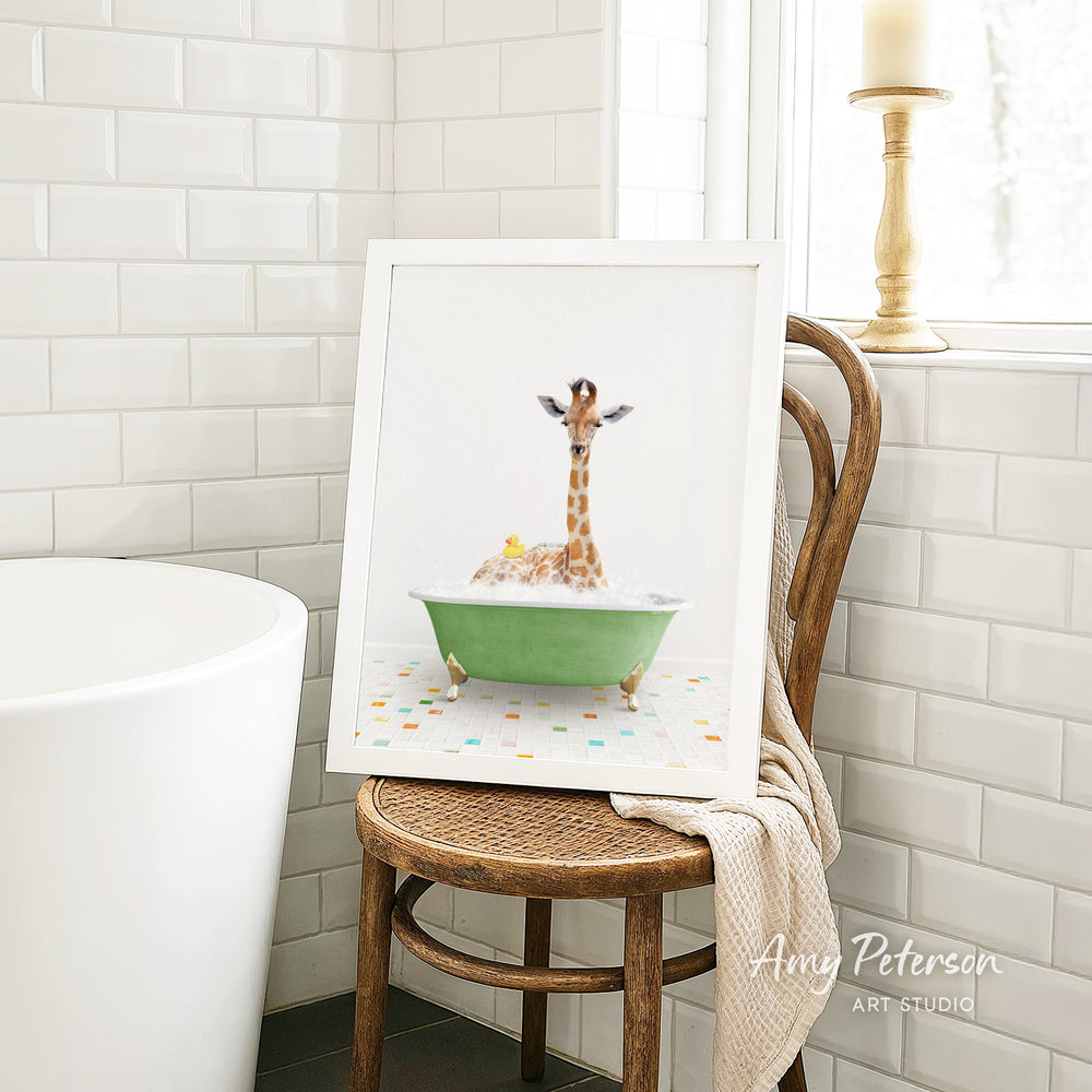 A framed image of a giraffe sitting in a green bathtub, surrounded by bubbles, is displayed on a wooden chair in a bathroom setting.