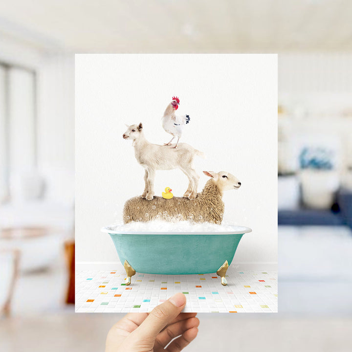 A hand holds up a framed image depicting a goat standing on a sheep's back while a chicken sits on top of a sheep in a bathtub.