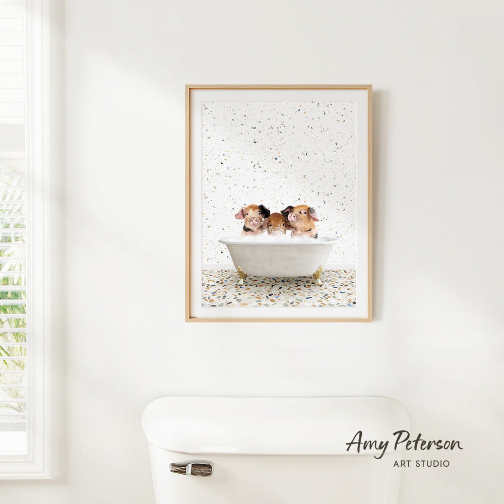 A framed print of three guinea pigs sitting in a bathtub is hanging on a white wall above a white toilet.