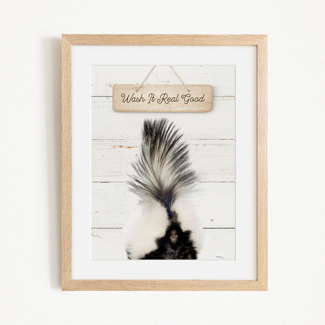 A framed image of a skunk's tail against a white wooden background, with a wooden sign above it that says "Wash It Real Good".
