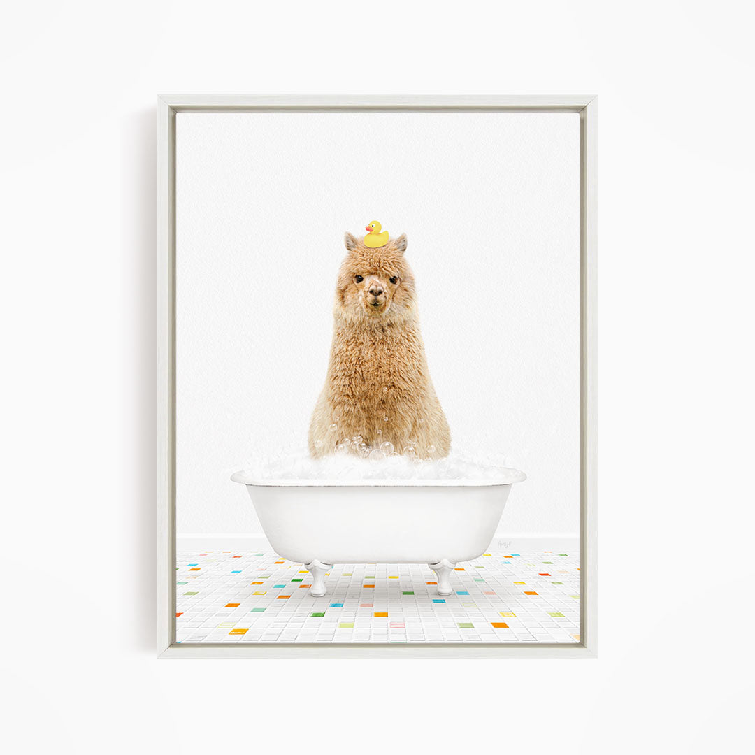 A fluffy brown llama sits in a white bathtub filled with bubbles, with a yellow rubber duck perched on its head.