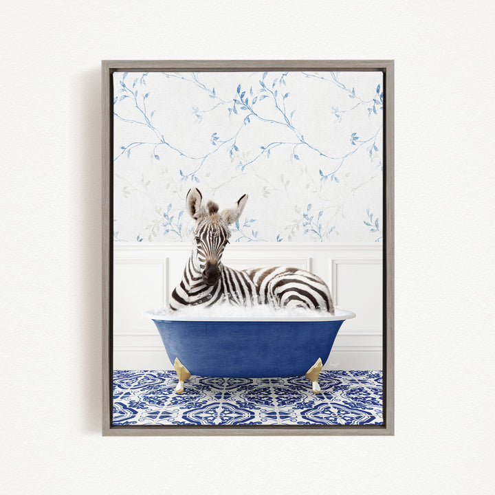 A zebra is sitting in a blue bathtub, surrounded by a blue and white patterned rug and a white wall with blue floral wallpaper.