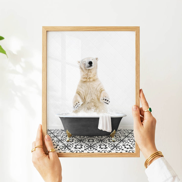 A person's hands are holding a framed picture of a polar bear sitting in a bathtub filled with water, surrounded by a black and white patterned tile floor.