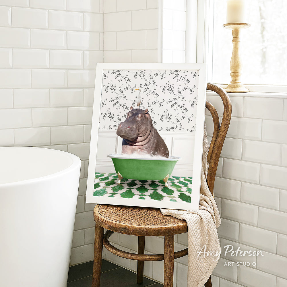 A framed image of a hippopotamus sitting in a green bathtub, surrounded by a patterned tile design, is displayed on a wooden chair in a bathroom setting.