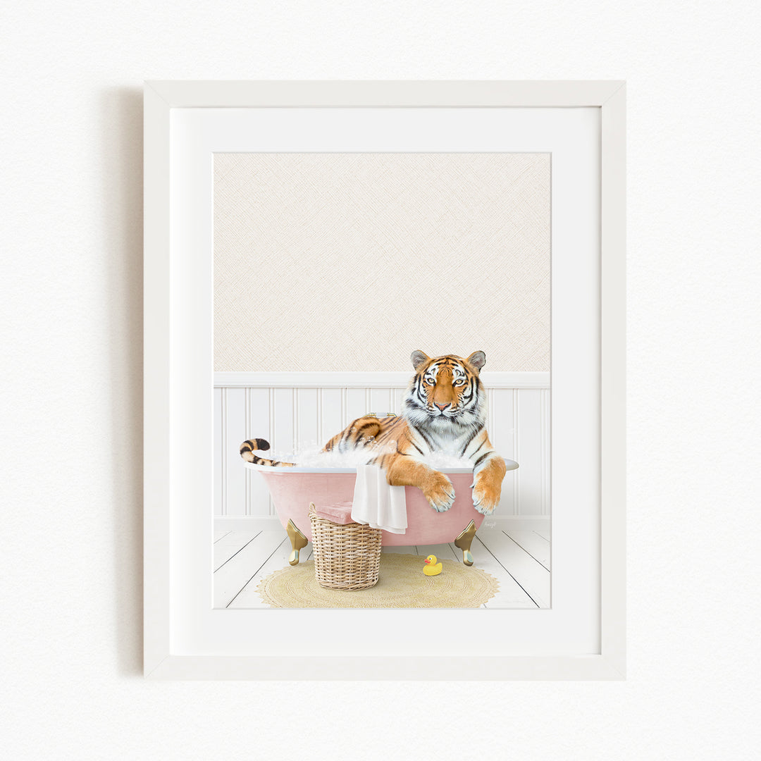 A tiger is sitting in a pink bathtub, surrounded by a yellow rubber duck and a basket.