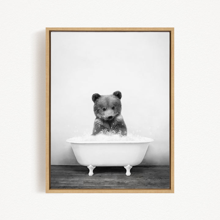 A black and white image of a bear sitting in a bathtub filled with water.