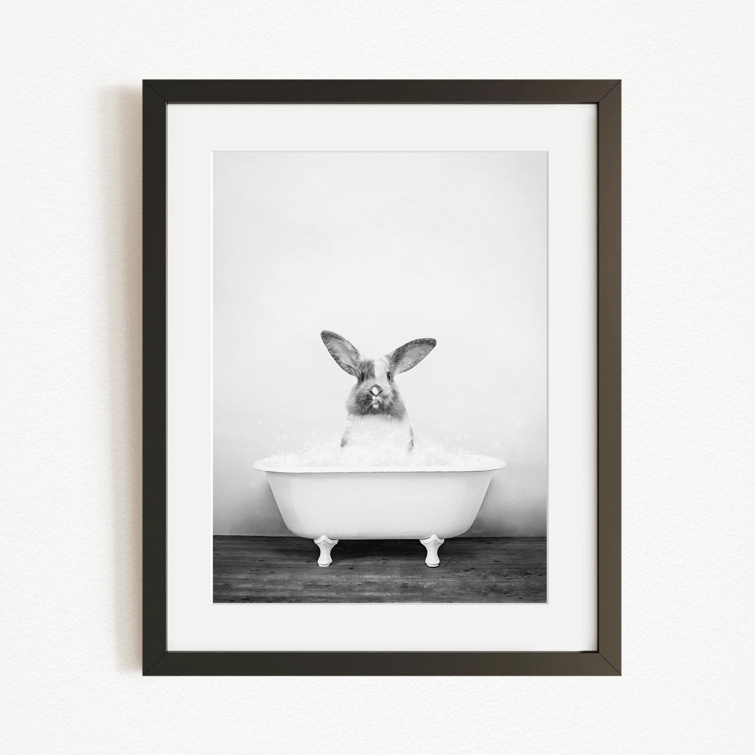 A black and white photograph of a rabbit sitting in a bathtub filled with water.