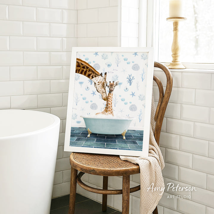A framed painting of two giraffes sitting in a bathtub, surrounded by blue and white floral patterns, is displayed on a wooden chair in a bathroom setting.