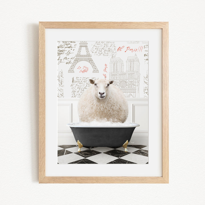A framed image depicting a fluffy white sheep sitting in a black bathtub, with a Paris-themed background featuring the Eiffel Tower and other Parisian landmarks.