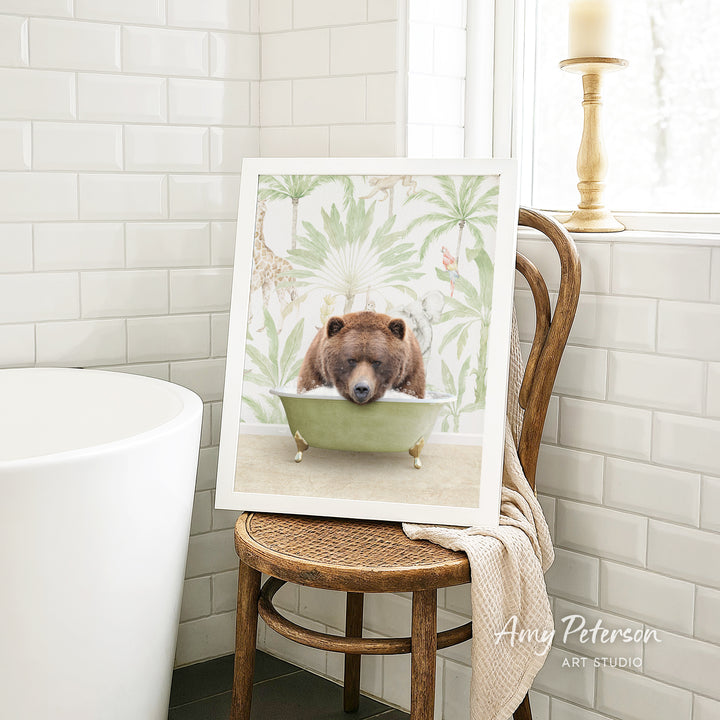 A framed image of a brown bear sitting in a bathtub, surrounded by tropical foliage, is displayed on a wooden chair in a bathroom setting.