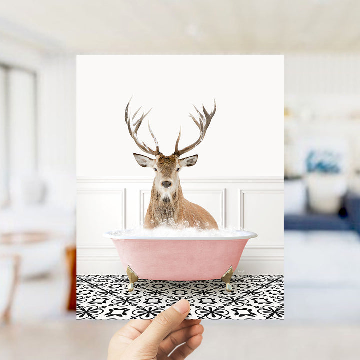 A deer with antlers is sitting in a pink bathtub filled with bubbles, creating a whimsical and unexpected scene.