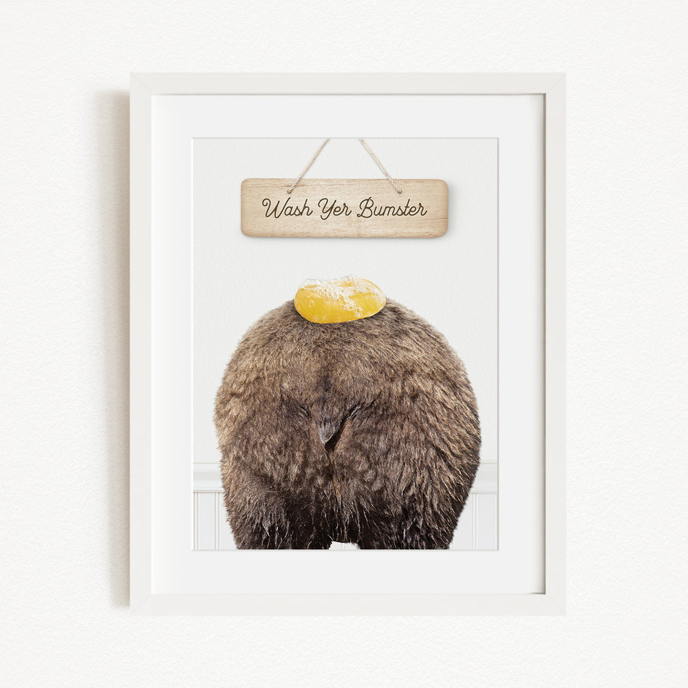 A framed image of a bear with a yellow object on its head, accompanied by a wooden sign that says "Wash Your Bummer".