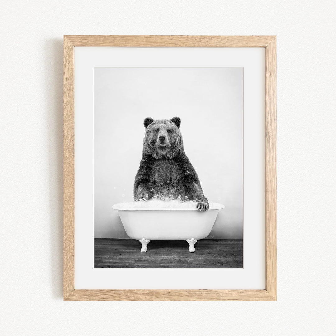 A black and white photograph of a bear sitting in a bathtub filled with water.