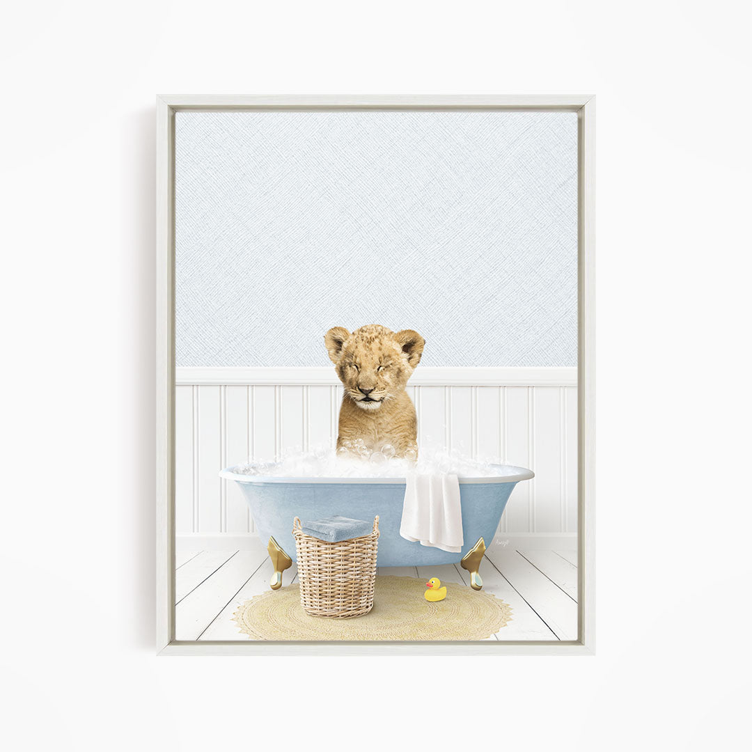 A young lion cub sitting in a blue bathtub filled with water, surrounded by a yellow rubber duck and a basket.