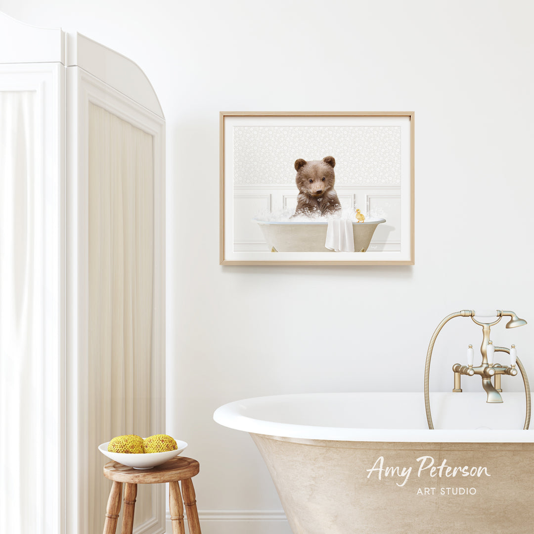 A framed image of a bear sitting in a bathtub is hanging on a white wall above a freestanding bathtub in a bathroom.