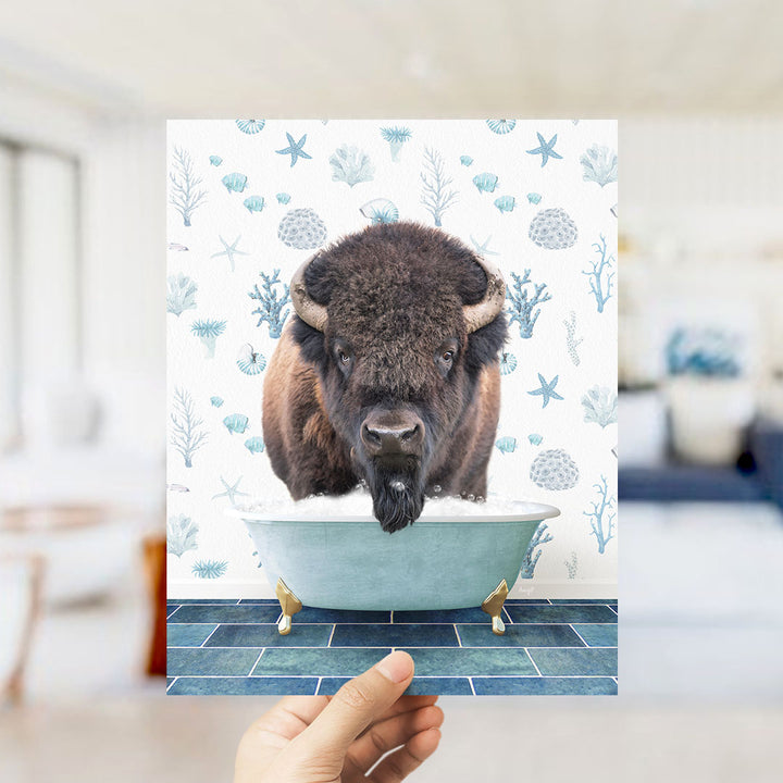 A hand is holding up a printed image of a bison in a bathtub, surrounded by a blue and white floral pattern.
