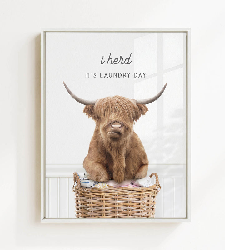 A brown cow with long horns is sitting in a wicker basket, with the text "i herd, it's laundry day" above the image.