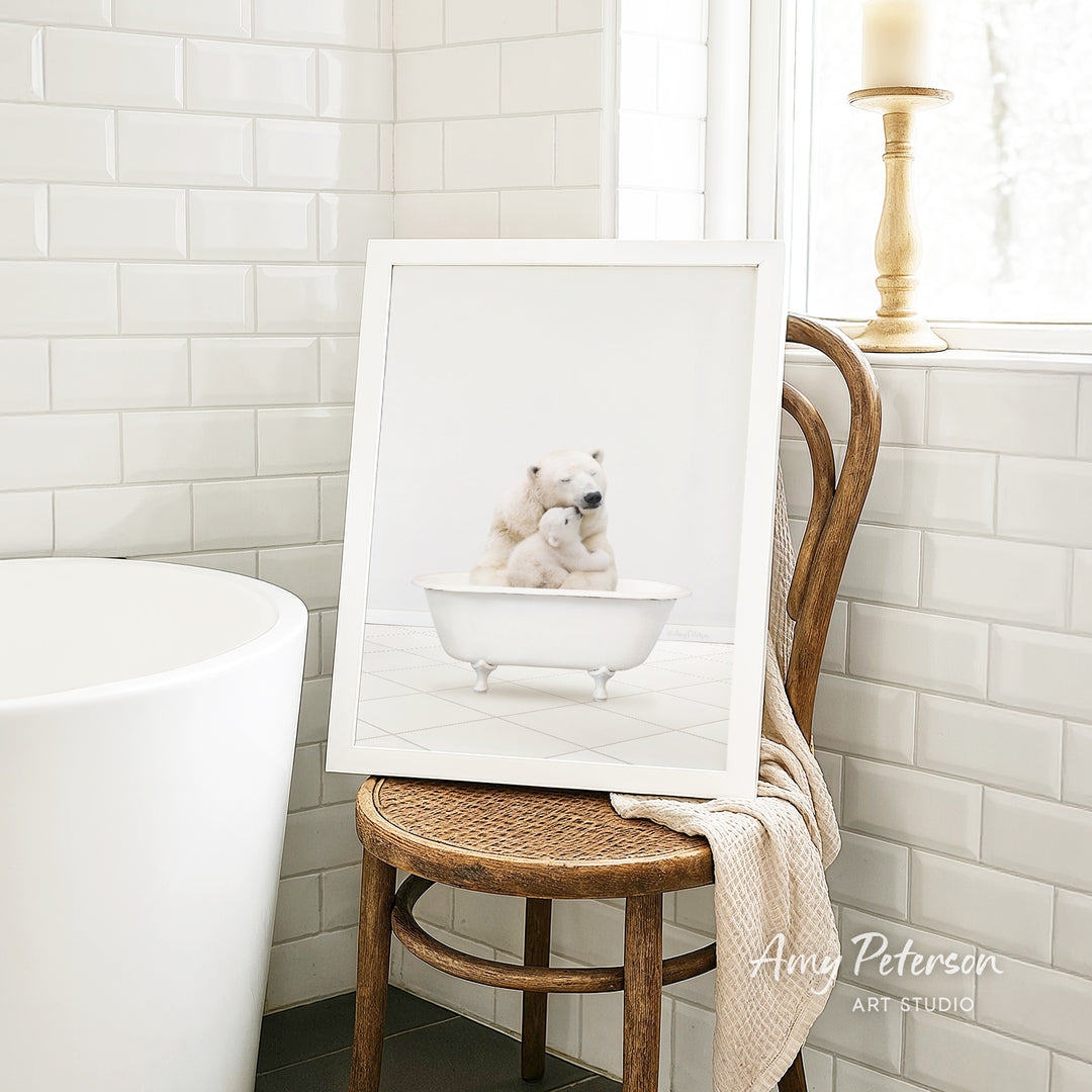 A framed image of two polar bears sitting in a bathtub is displayed on a wooden chair in a bathroom setting.